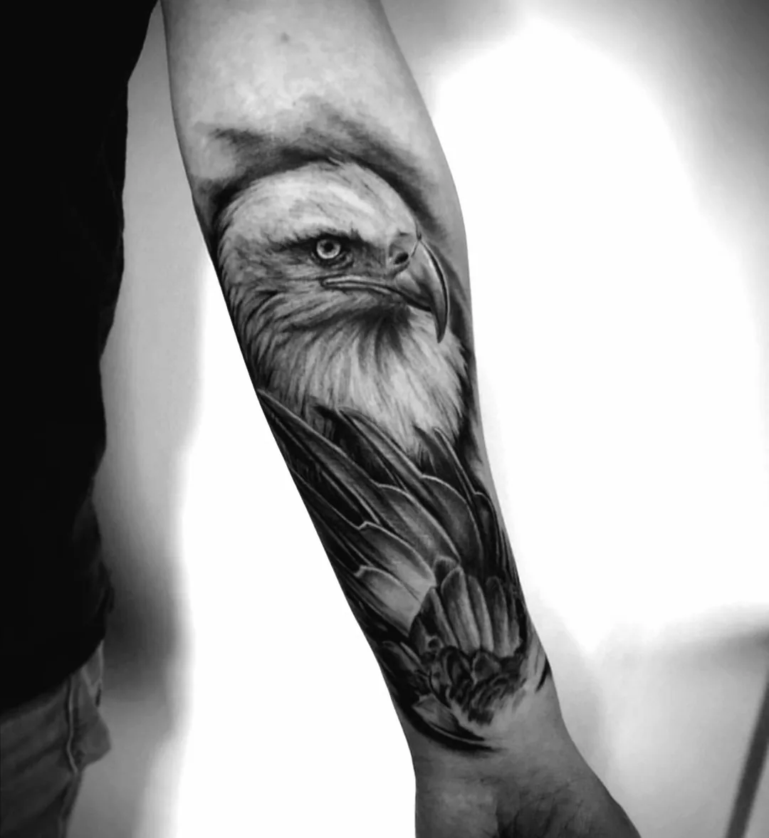 Black-and-grey eagle above a lotus, tattooed on a forearm.